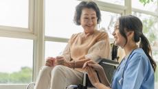 A caregiver kneeling beside a senior patient on a wheelchair