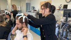 A therapist-in-training putting on the SynPhNe device on a volunteer's head