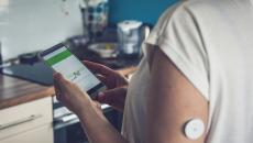 Woman checking glucose level with a remote sensor and mobile phone