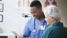 A doctor and a patient look at a tablet in his office.