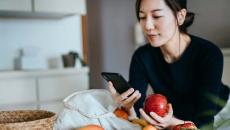 Person leaning against a counter holding an apple while looking at their phone