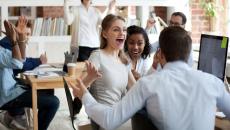 Three people with arms raised celebrating around computer monitor