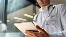 Doctor holding a tablet while in a lab coat with a stethoscope around their neck 