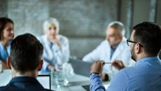 Group of people, two in lab coats, sit around table 