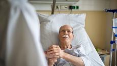 person in hospital bed holds hand of person in white lab coat