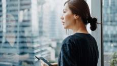 Person looking out the window while holding a mobile phone