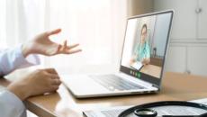 Person in lab coat talking with hands to nurse on laptop