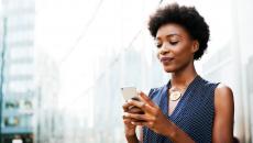 Person standing outside while looking at a phone with the appearance of a city behind her