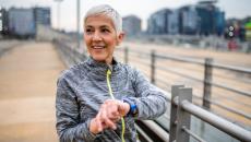 Person standing on a boardwalk while holding their wrist with a smartwatch on it