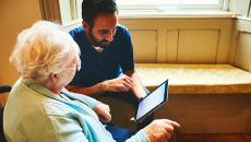 An aide helps a senior operate a tablet device