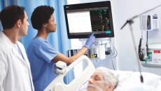 Providers using the new patient monitor next to a bed where a patient is sleeping