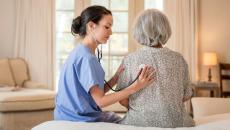 A nurse using a stethoscope on an older patient in her home.