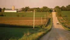 A truck driving on a gravel road near a farm