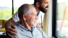 Person sitting in a wheelchair with a healthcare provider next to them, looking out a window