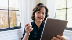 Person on a tablet holding a prescription bottle in their hand while sitting next to a window