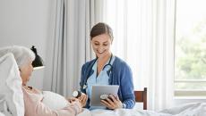 Healthcare provider in a patient's home sitting next to a patient lying in bed