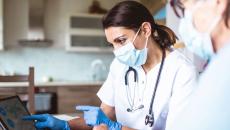 Healthcare provider wearing a mask while talking to a patient and showing them something on a computer screen