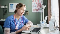 Healthcare provider in scrubs sitting at a desk and looking at a computer