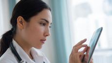 Healthcare provider wearing a lab coat and a stethoscope while interacting with a tablet