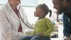 Healthcare provider examining a patient while their caregiver stands nearby watching