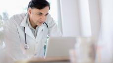 Healthcare provider leaning on a desk and looking at a computer