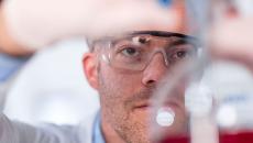 Scientist in a laboratory filling up a beaker while wearing safety goggles