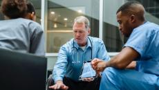 Three healthcare providers sitting around a table looking at a tablet