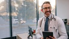 Healthcare provider sitting on a desk holding a tablet while smiling 