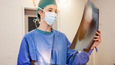 Healthcare provider in scrubs wearing a mask and looking at a large diagnostic image