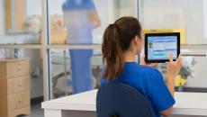 Healthcare provider in the clinical setting sitting at a desk and looking at a tablet