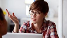 Person sitting at a computer with their hand up talking 