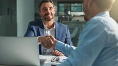 Two people sitting on opposite sides of a desk while shaking hands