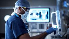 Healthcare provider wearing scrubs and a face mask while looking at screens with diagnostic images on them