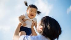 Person holding another little person above their head with the sky in the background