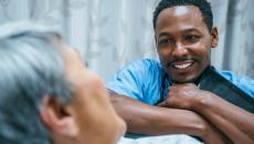 Nurse leaning against a patient's bed while the patient looks at them