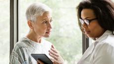 An elderly patient talking to a doctor who is holding a tablet