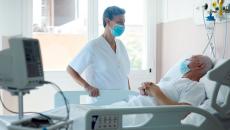 Person in mask standing over person in hospital bed