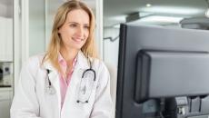 A doctor checking a patient's medical record on a desktop computer