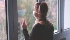 A woman wearing a mask looking out a window