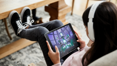 Person sitting on a couch with their feet up while wearing headphones and looking at a tablet